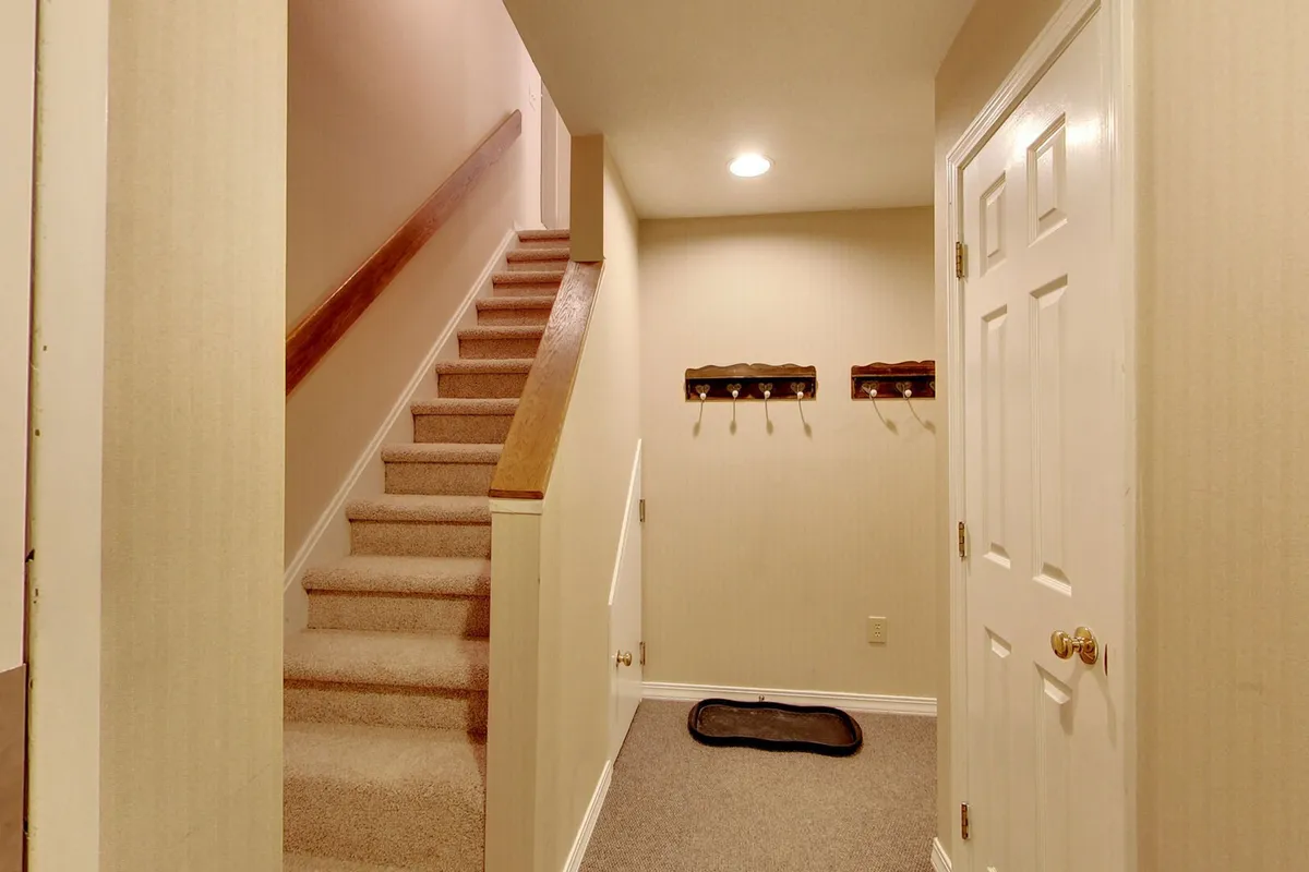 A welcoming interior entryway featuring a staircase, coat hooks for ski gear, and an inviting rug. The space is filled with natural light, creating a warm first impression for those coming inside after a day on the slopes.