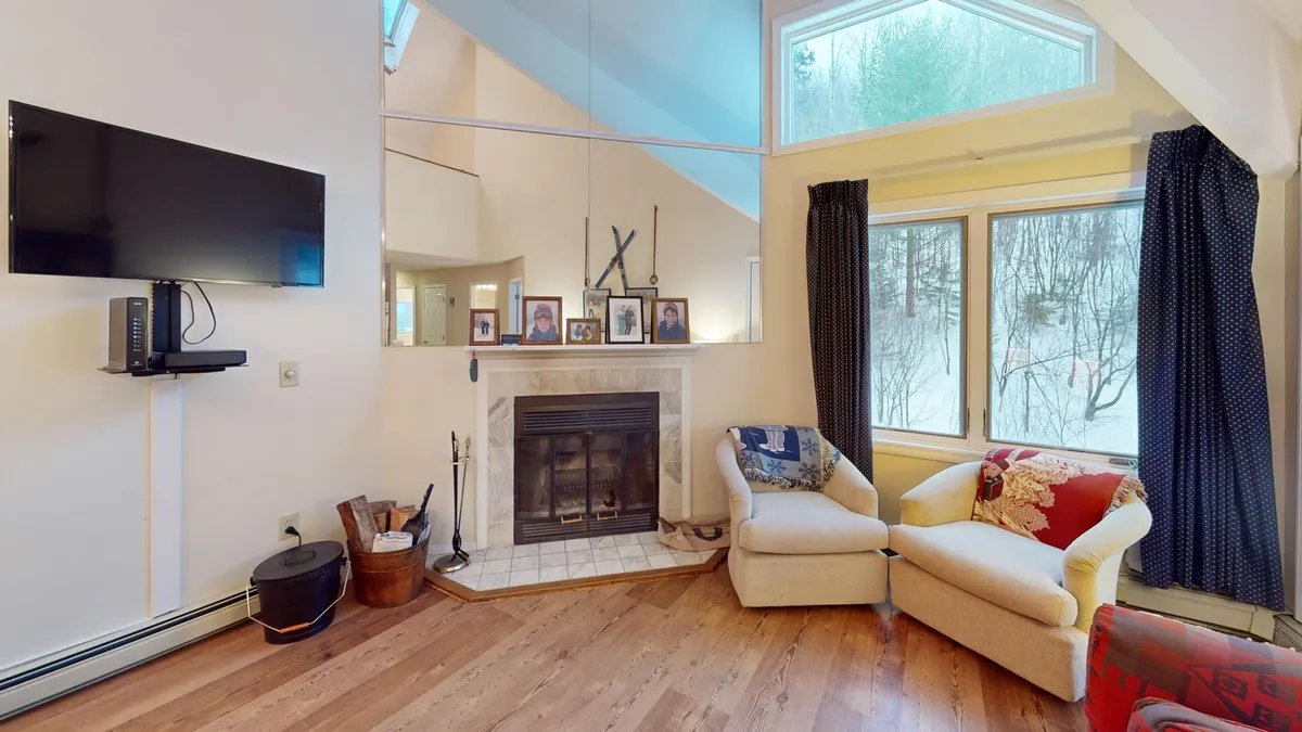 A warm living space centered around a stately fireplace, with plush seating, large windows that frame mountain views, and a prominent flat-screen TV. The arrangement suggests an ideal spot for movie nights or cozy evenings sharing stories.