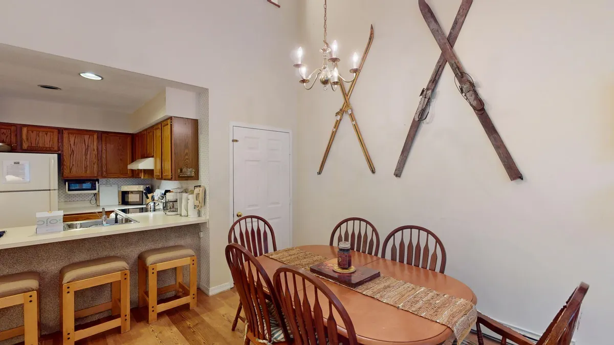 A dining area with a central table, a warm chandelier overhead, and ski equipment tastefully displayed on the wall. The setting is designed for gatherings, meals, and socializing, creating a lively hub for guests to connect and share stories after time on the mountain.