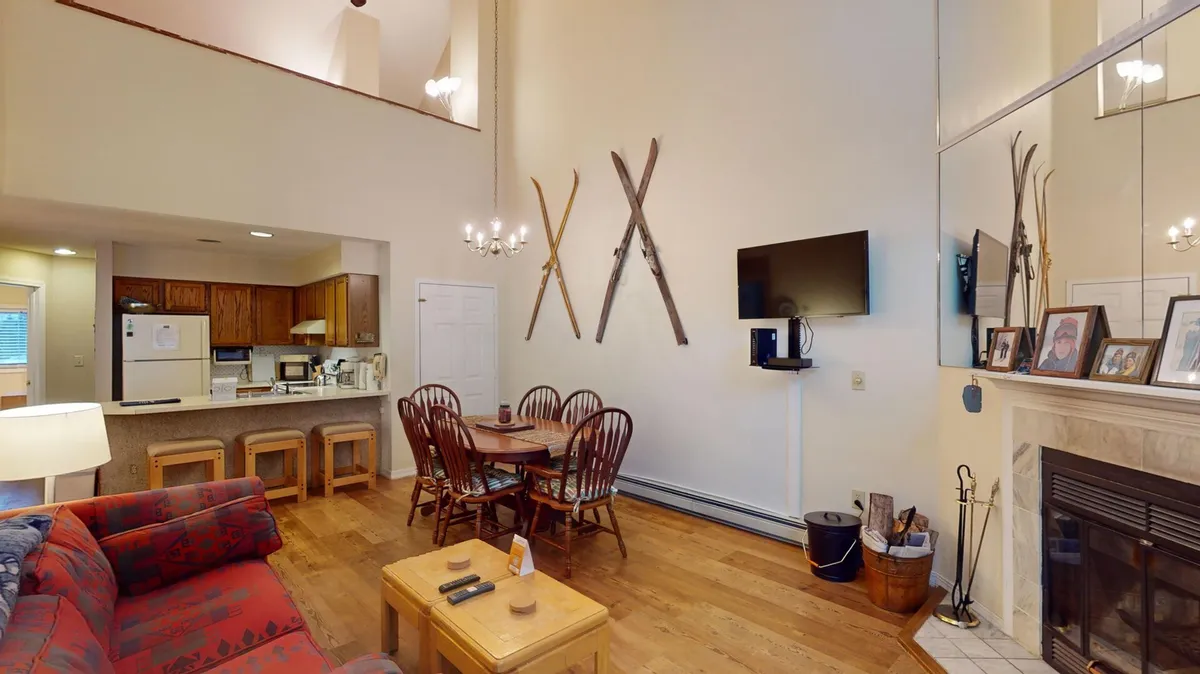 A cozy living area with a patterned sofa, wooden dining table, fireplace, and decorative skis mounted on the wall, capturing the ambiance of a mountain retreat. The space is designed for gatherings and unwinding after outdoor activities.
