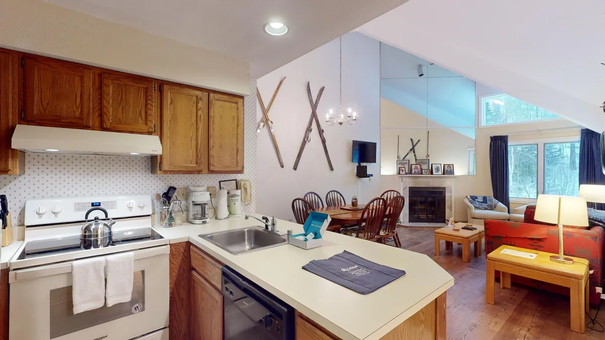A cozy, communal kitchen and dining space blends seamlessly with a fireside lounge area. Large windows frame views of the snowy outdoors, while the open layout invites group cooking, dining, and socializing.