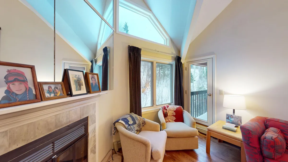A spacious living area featuring a wood-burning fireplace, comfortable seating, large windows framing views of the outdoors, and touches of personal decor such as family photographs. The scene exudes warmth and invites relaxation, suggesting a welcoming spot to gather after a day on the slopes.