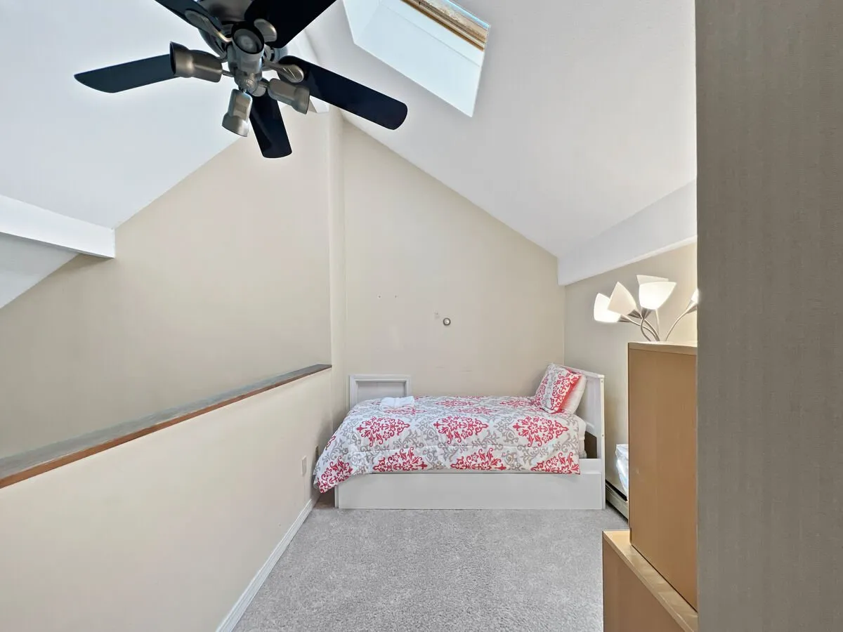 An inviting bedroom with patterned bedding, a ceiling fan, and a lamp. Soft sunlight filters in, creating a soothing, restful mood ideal for unwinding after a day of adventure or wellness activities.