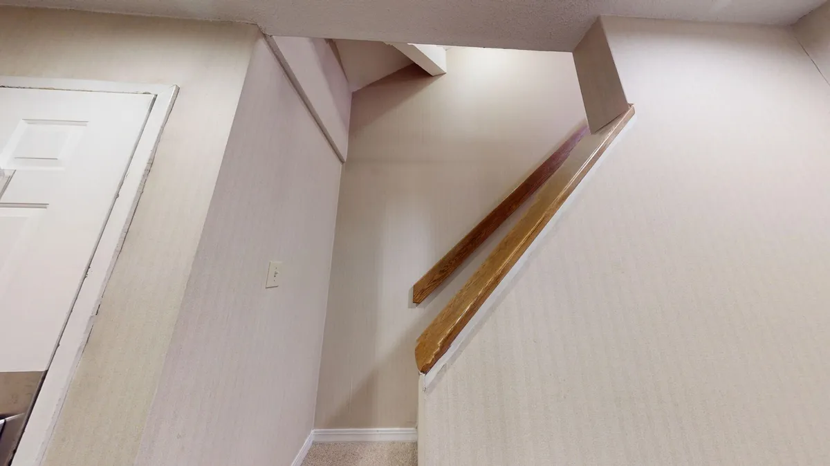 A view of a staircase leading upwards with softly lit walls and a door at the top. The scene hints at exploration and the discovery of a hidden nook, suggesting the open loft area described in the section.