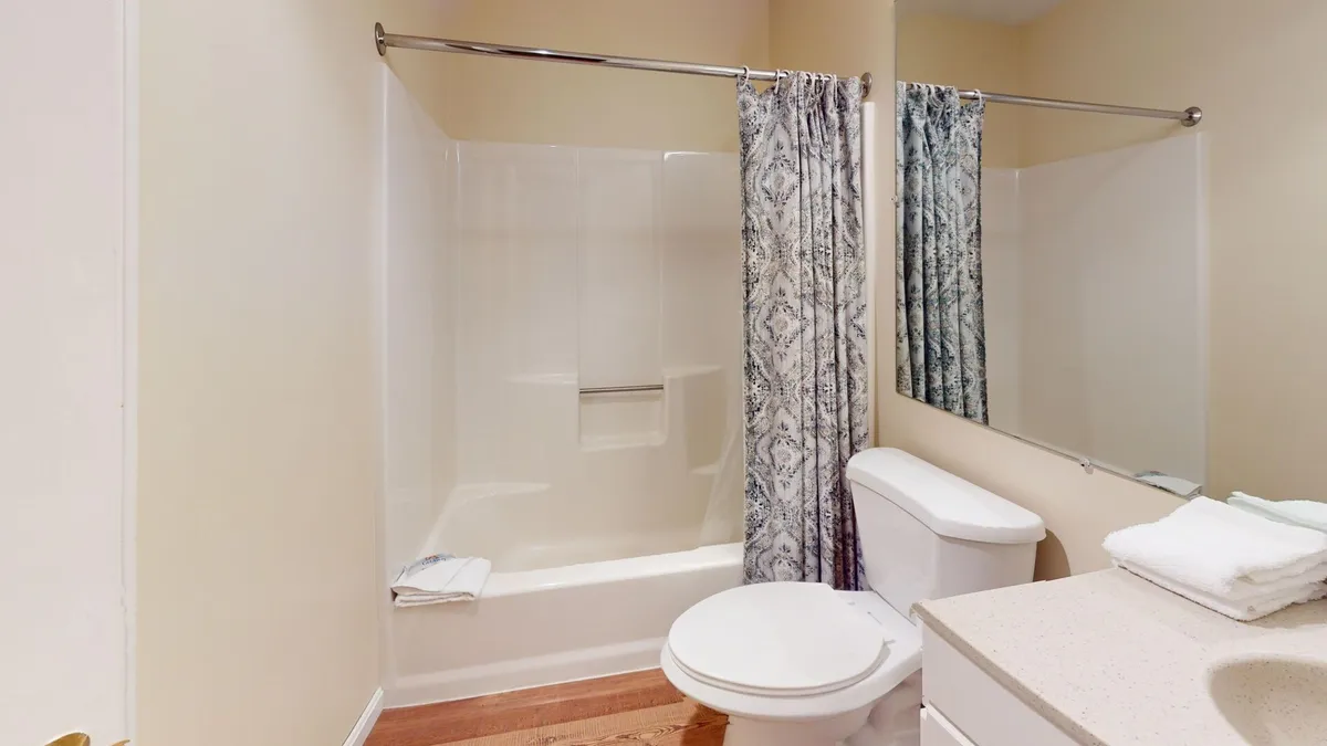 A serene bathroom interior featuring a bathtub, vanity with mirror, toilet, and a simple curtain. The atmosphere is calming, providing a private retreat for bathing and relaxation after an active day.