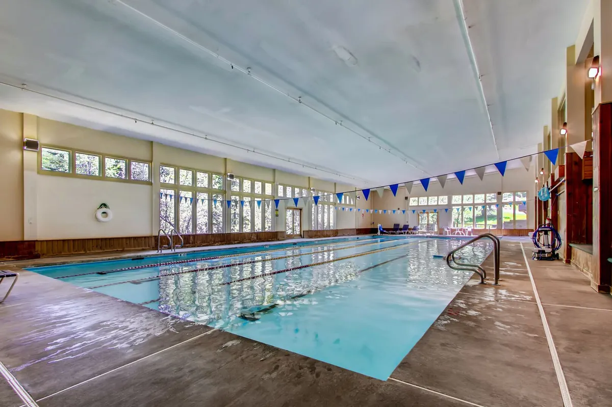 This interior image captures a vibrant pool area featuring a spacious swimming pool, large windows allowing natural light to flood the space, blue bunting flags adding a festive touch, and a poolside seating area for relaxation. The atmosphere is both refreshing and social, ideal for all-season leisure and family gatherings.