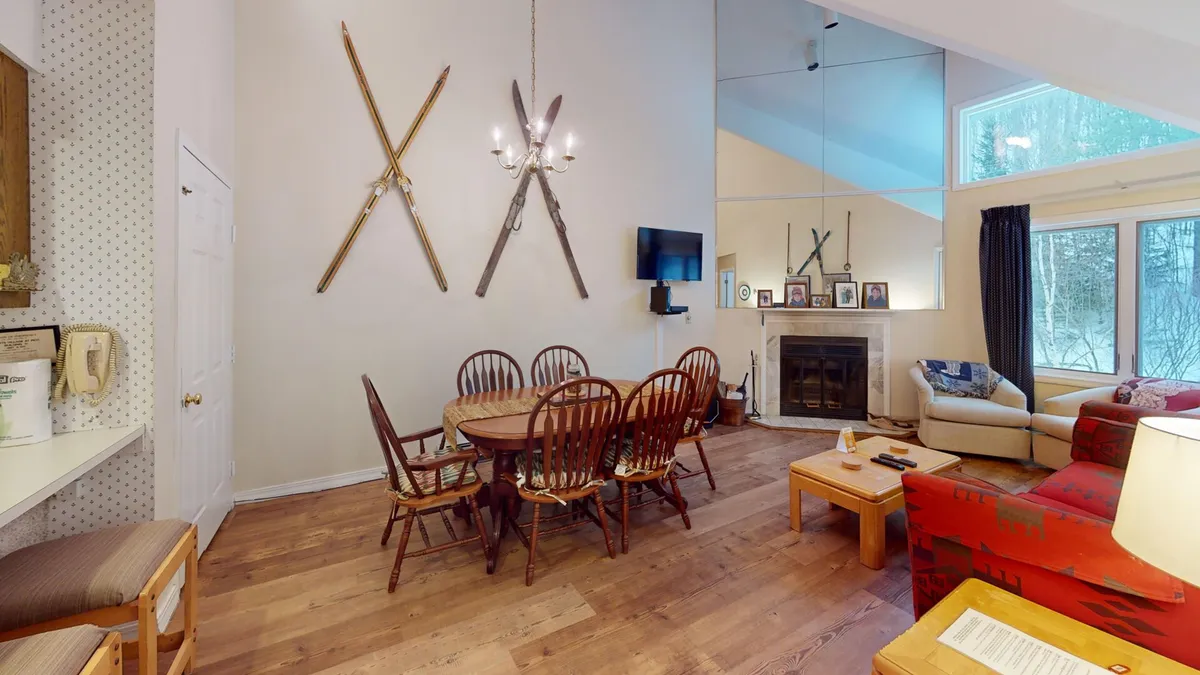 A welcoming dining area with a sturdy wooden dining table surrounded by chairs, adjacent to a fireplace and a TV. Decorative skis on the wall add a mountain lodge feel, while the space is clearly designed for shared meals and game nights.