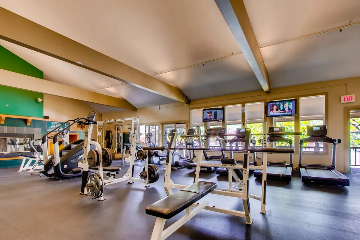 A well-equipped exercise room is shown, outfitted with treadmills, various exercise machines, large windows for natural light, and television screens to keep workouts engaging. The space is modern and motivational, inviting residents to maintain their fitness routine.