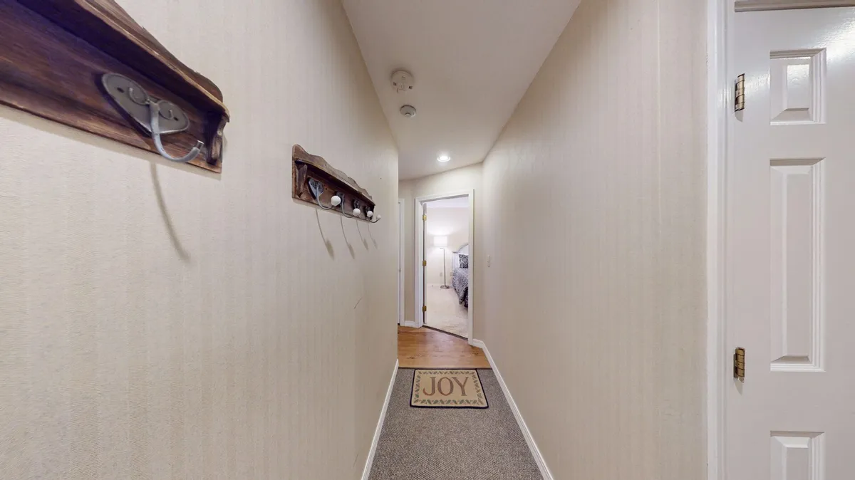 An inviting hallway scene with a welcome mat and open doorway, giving a sense of arrival and transition from outside to in. The image captures the anticipation of entering a welcoming mountain retreat after a day on the slopes.